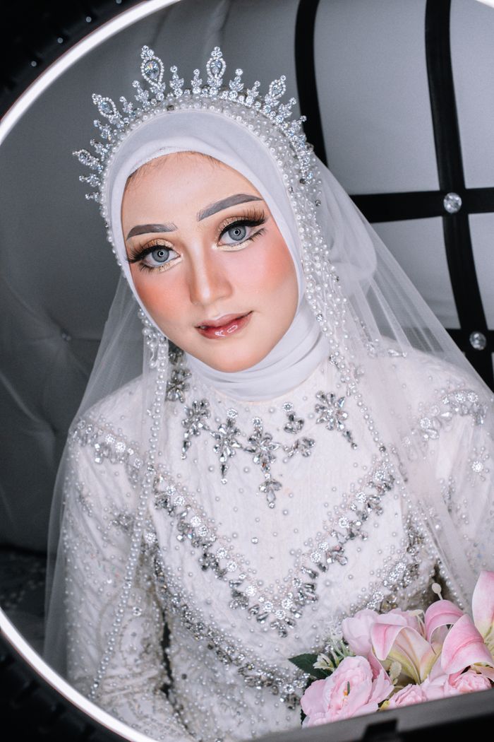 Beautiful Muslim bride in sparkling gown, holding pink bouquet. Captures elegance and joy.
